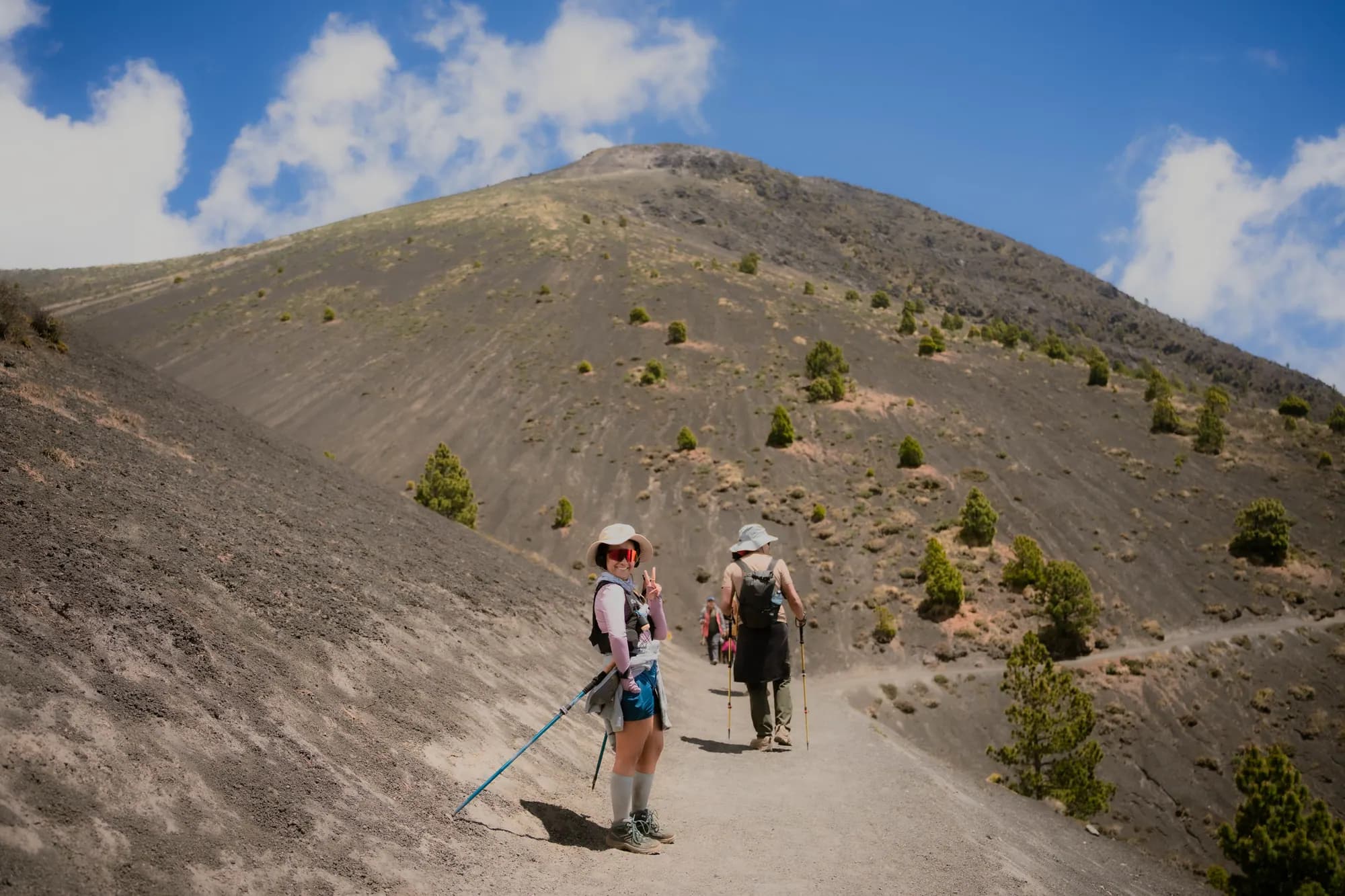 Two hikers on the volcanic sand trail under a blue sky