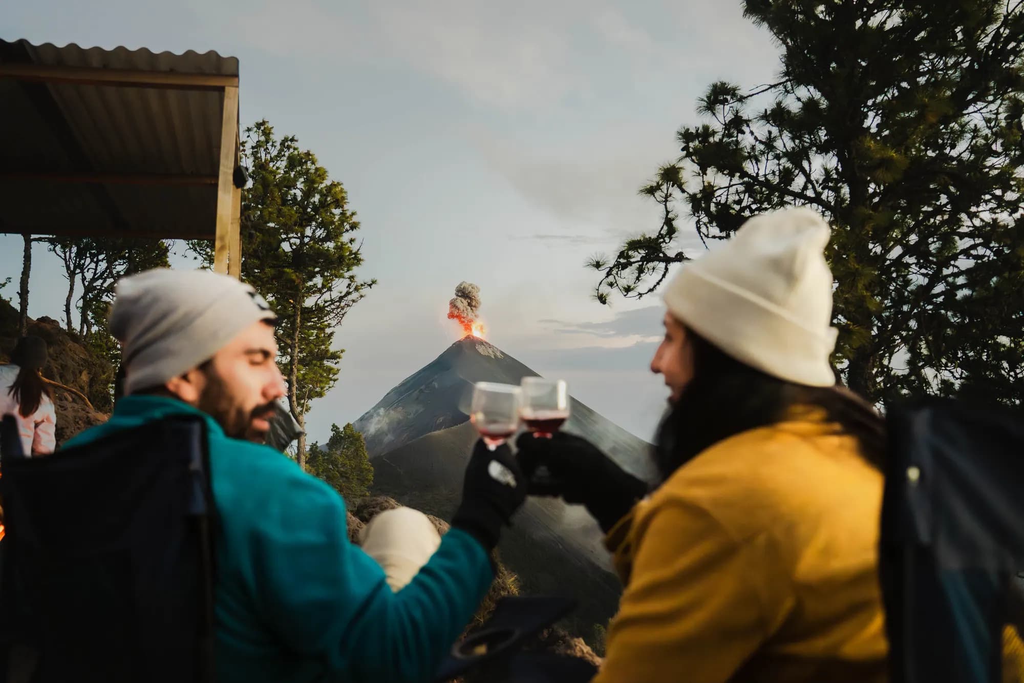 Two travelers toasting at camp while Fuego erupts