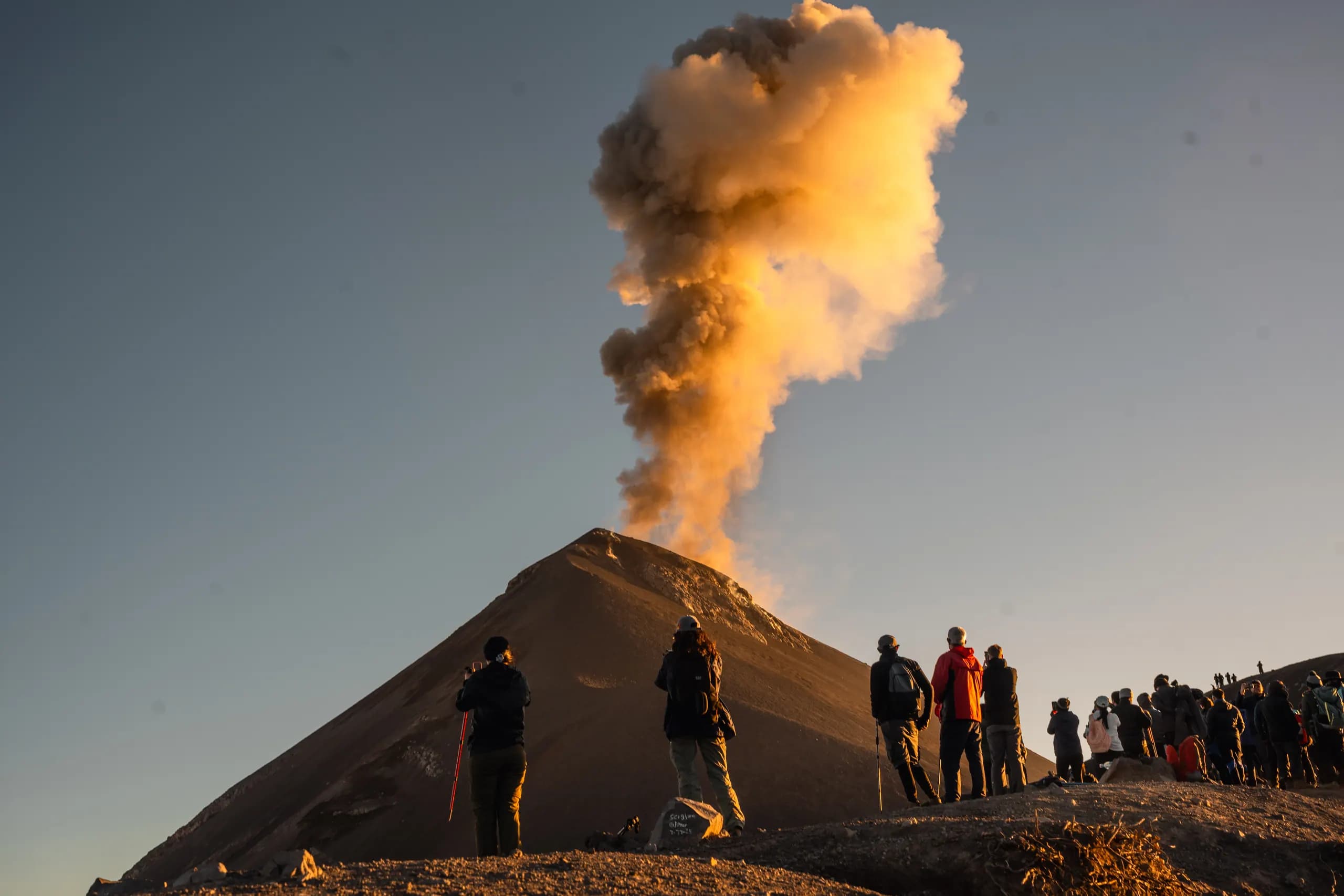 A line of hikers watching Fuego erupt at sunrise