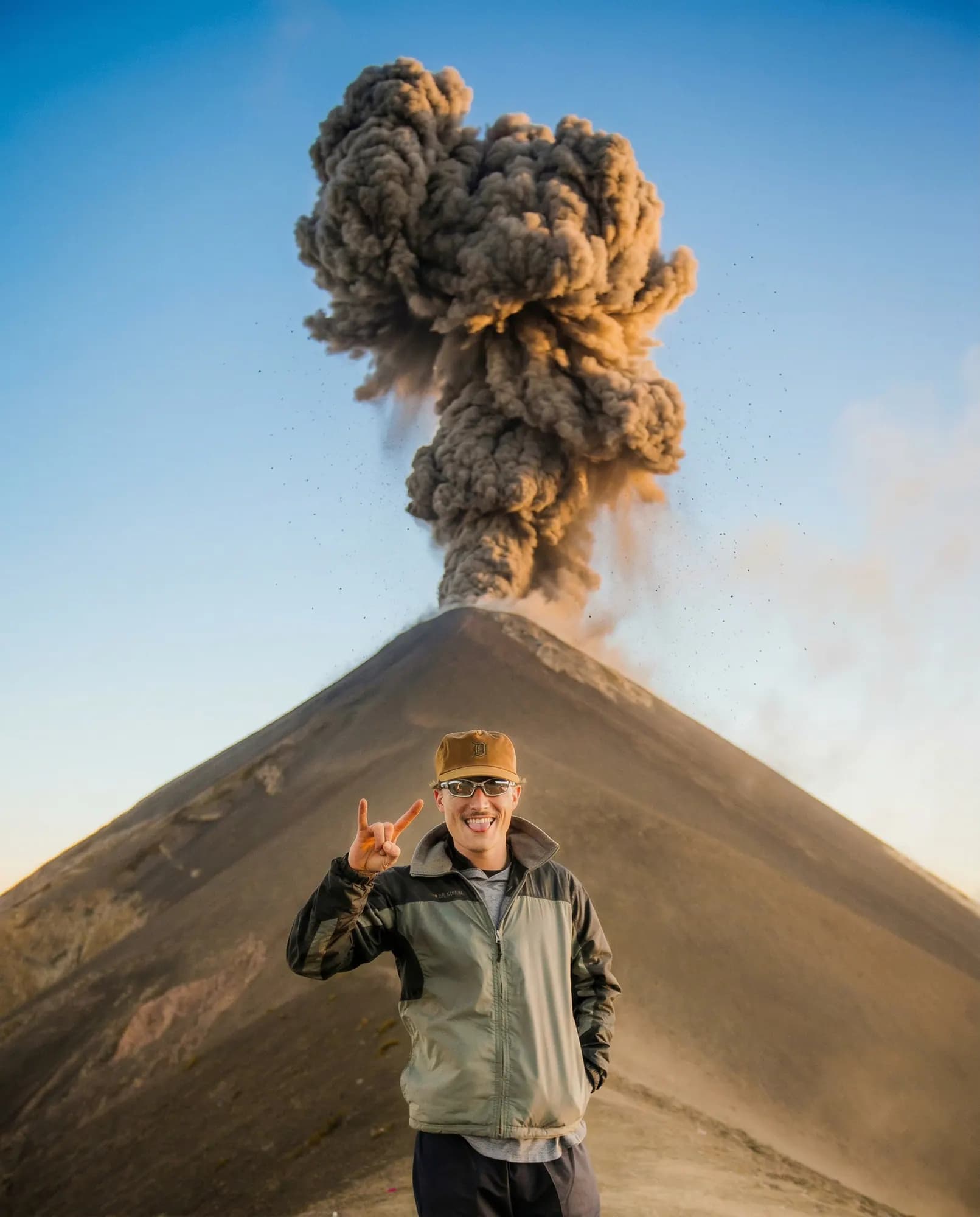 A hiker waving while Fuego erupts behind him