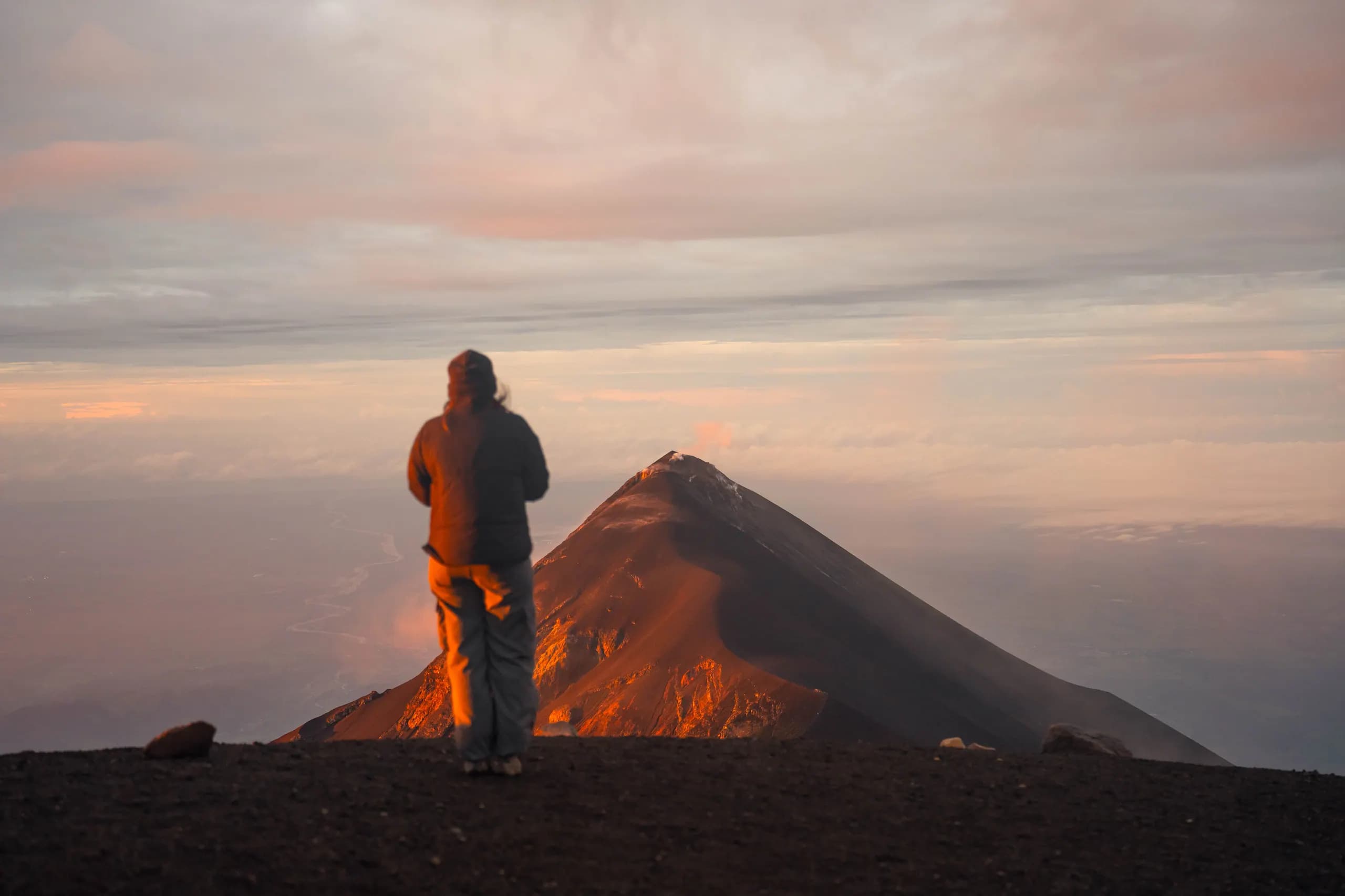 A hiker in an orange jacket in front of Fuego's glow