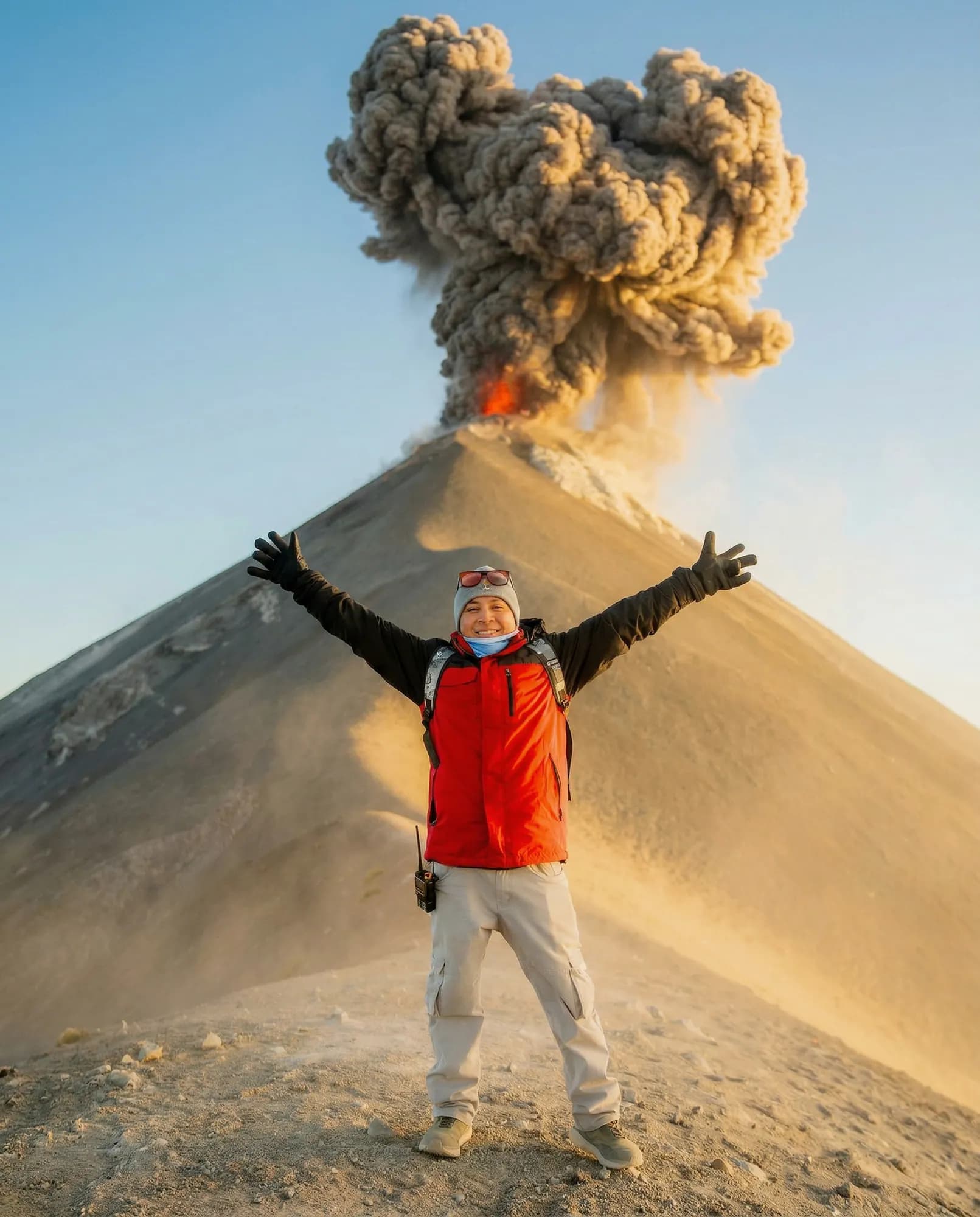 A hiker with open arms in front of an eruption of Volcán de Fuego