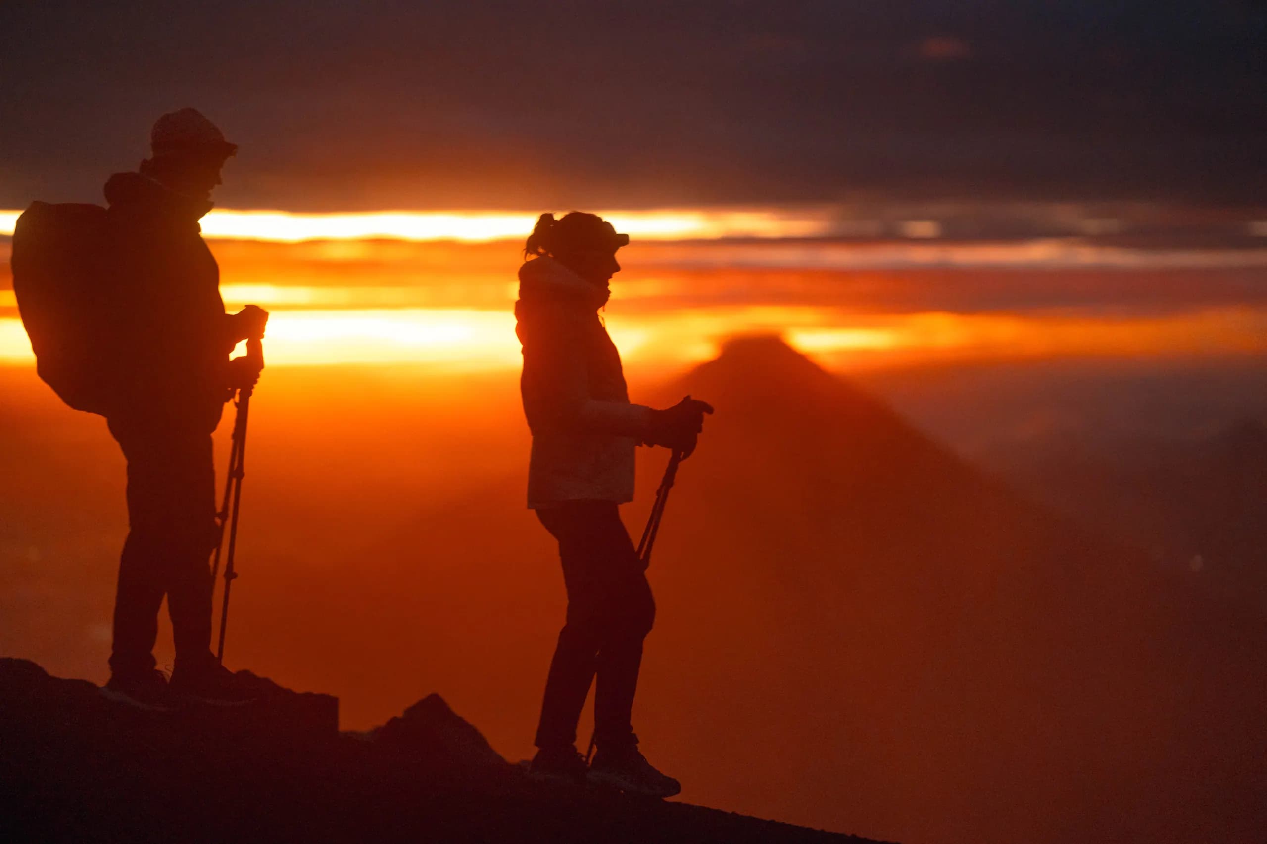 Two hikers silhouetted against an orange sunrise